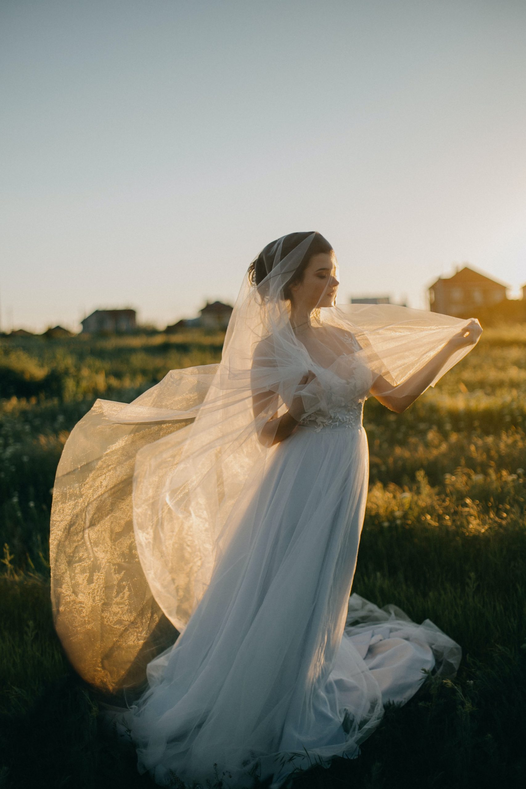 "A beautiful bride stands confidently with a proud smile on a sunny and windy day, with her veil blowing in the breeze."